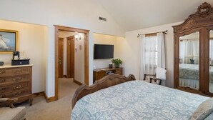 A bedroom with a large bed, a dresser, a television, and a mirror. - Sunflower Hill Inn (Moab)