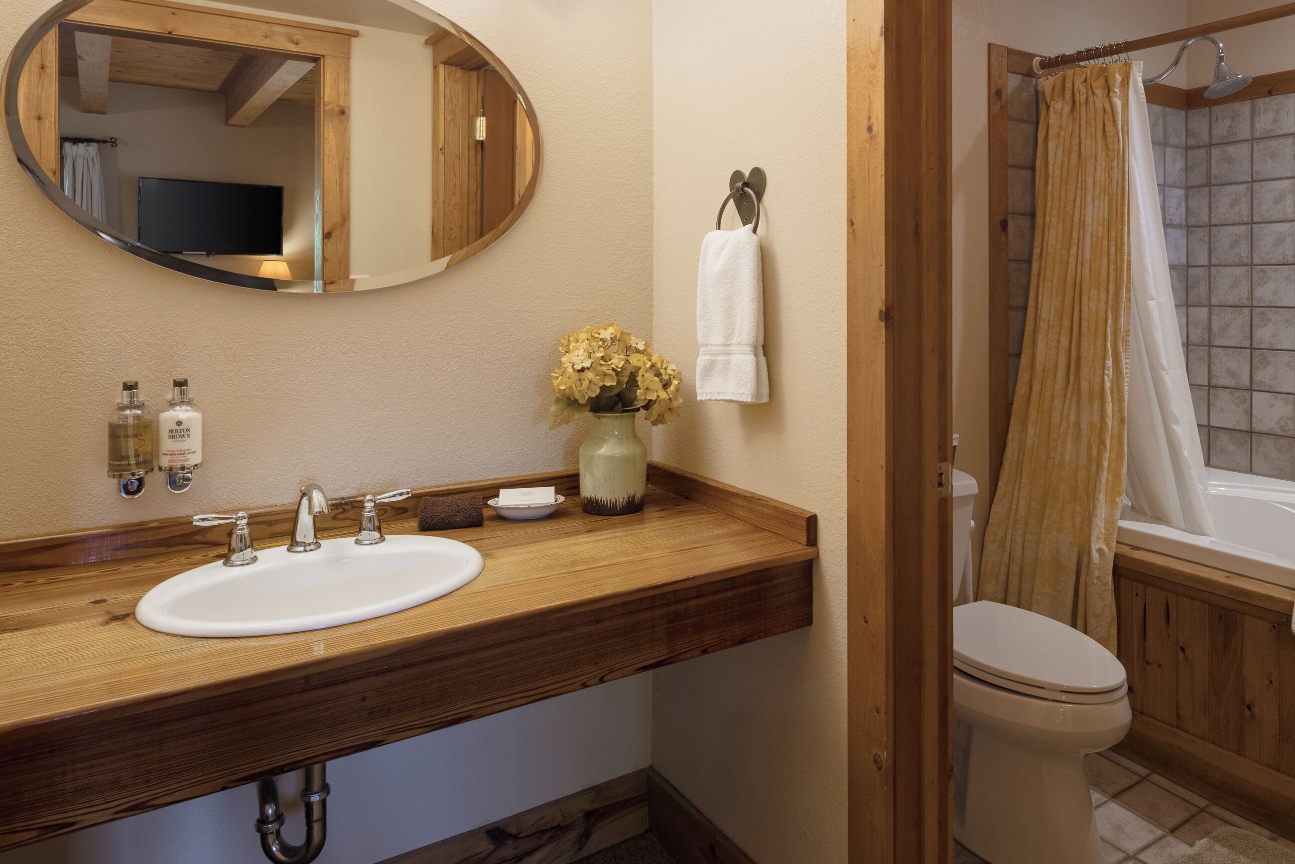 A bathroom with a wooden vanity, a sink, a mirror, a toilet, and a shower curtain.