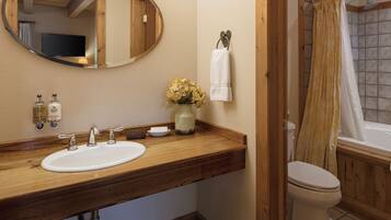A bathroom with a wooden vanity, a sink, a mirror, a toilet, and a shower curtain.