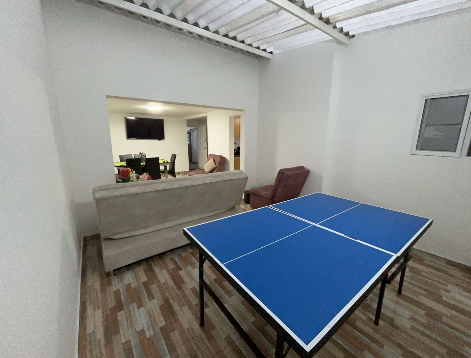 A room with a ping pong table, a sofa, and a TV mounted on the wall.