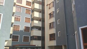 Un immeuble résidentiel à plusieurs étages, doté de balcons, d’une entrée sécurisée et d’une cour dallée.