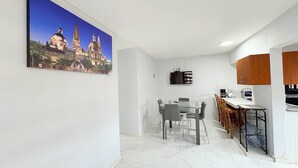 Μια σύγχρονη κουζίνα με τραπεζαρία, λευκούς τοίχους και έναν μεγάλο πίνακα που απεικονίζει ένα ιστορικό κτίριο.