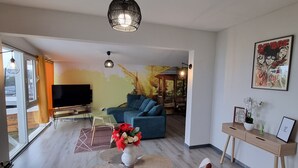 Ein modernes Wohnzimmer mit Sofa, Esstisch mit Stühlen, Fernseher und einem Gemälde an der Wand.