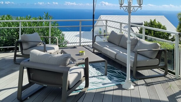 Eine Terrasse mit Gartenmöbeln, einem großen Sonnenschirm und Blick auf den Ozean.