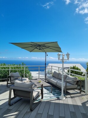 Eine Terrasse mit Gartenmöbeln, einem großen Sonnenschirm und Blick auf den Ozean.