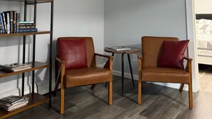 Une pièce comprenant deux fauteuils en cuir marron, une petite table ronde et une bibliothèque avec des livres et une plante.