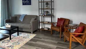 Un salon moderne avec un canapé gris, une table basse en bois, un tapis à motifs, une bibliothèque et un ventilateur de plafond.