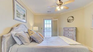 Une chambre à coucher avec un lit, un ventilateur de plafond, une commode et une porte avec des volets.