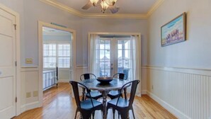 Une salle à manger avec une table ronde, quatre chaises, un ventilateur de plafond et une fenêtre avec des rideaux.