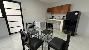 A compact kitchen with a glass dining table, wooden chairs, a black refrigerator, and wooden cabinets. - Residencia Gran Coyula Orange 504A (Tonala)