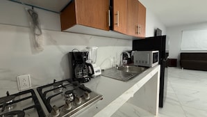 A kitchen with a gas stove, a coffee maker, a microwave, and wooden cabinets. - Residencia Gran Coyula Orange 504A (Tonala)