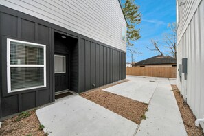 A modern building with a dark exterior and white siding, a concrete pathway, and a wooden fence in the background. - Houston Townhome NRG, Med Center, Downtown, Free Parking (Houston)