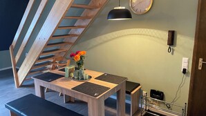 Un coin repas avec une table en bois, des bancs, un vase de fleurs, une horloge et un téléphone fixé au mur.