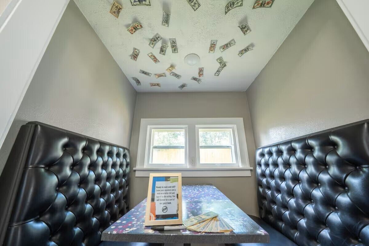 A room with a high ceiling, two windows, and a table with a sign.