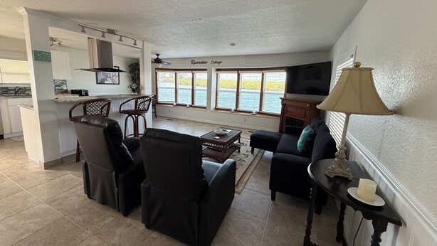 Amplia sala de estar con cocina, comedor y ventanas grandes con vistas al agua.