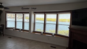 Una sala de estar con chimenea, televisor y vistas a un río a través de amplios ventanales.