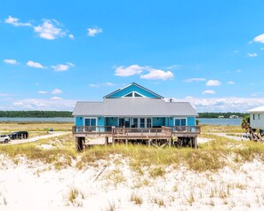 A beachfront house with a blue roof and wooden deck, overlooking a sandy beach and a body of water. - NEW! Beachfront 6BR Home With Panoramic Gulf Views, Game Room, Sleeps 26 (Gulf Shores)