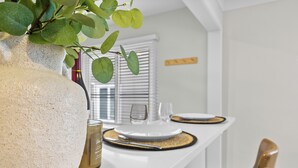Et spiseområde med et hvidt bord dækket til to, en vase med grønne blade og en flaske vin.