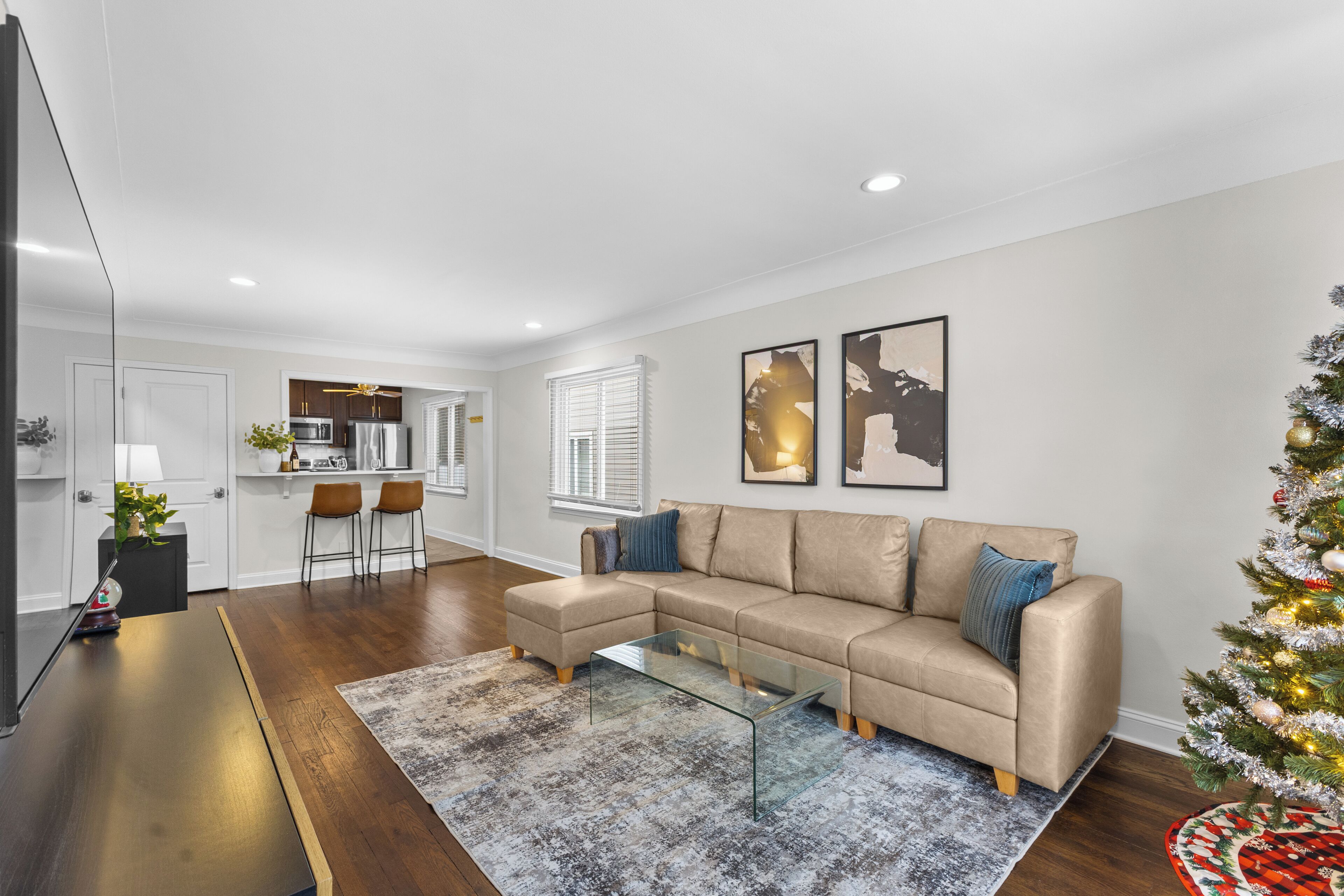 A modern living room with a beige sectional sofa, a glass coffee table, and a small Christmas tree.