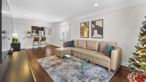En moderne stue med en beige hjørnesofa, et glasbord og et lille juletræ.