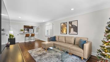 A modern living room with a beige sectional sofa, a glass coffee table, and a small Christmas tree.