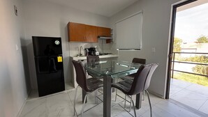 A modern kitchen with a glass dining table, two chairs, a refrigerator, and a stove. - Residencia Gran Coyula Orange 508B (Tonala)