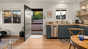 Eine moderne Küche mit Spülmaschine, ein Essbereich mit Holztisch und -stühlen sowie Blick auf einen Garten durch eine offene Tür.