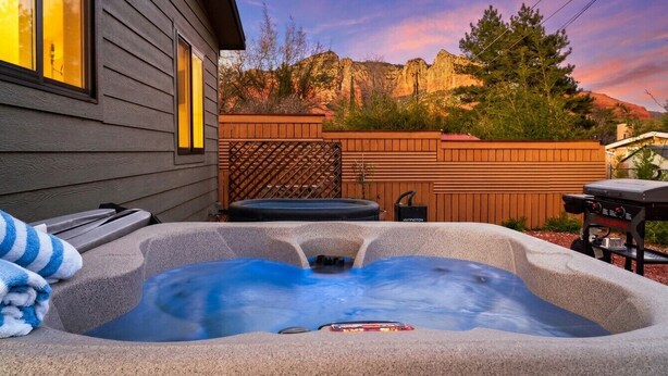 Ein Whirlpool in einem Garten mit Holzzaun, Grill und einem Haus im Hintergrund.