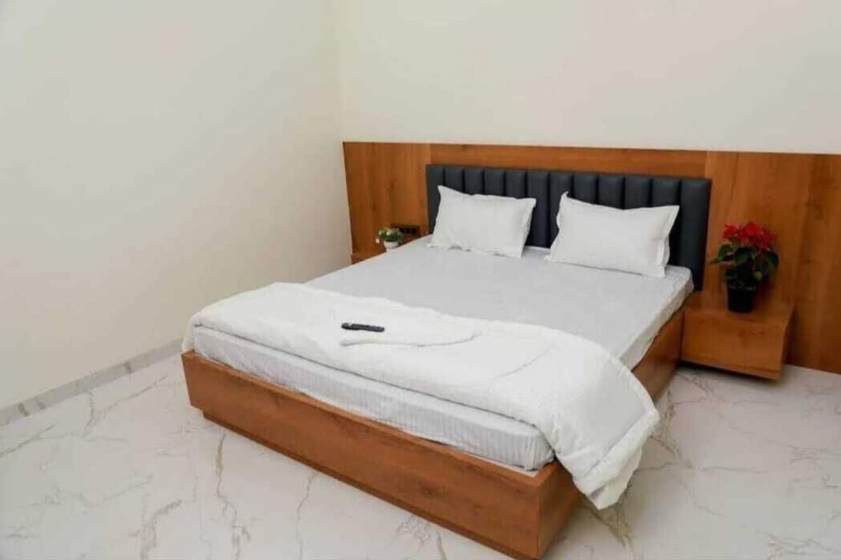 A neatly made bed with a wooden headboard, white bedding, and a small bedside table with a red flower.