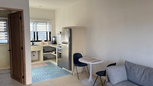 A modern kitchen with a refrigerator, sink, and window. There is a dining area with a table and chairs. - BRIGHT & COZY 1-KING BEDROOM CASITA WITH QUEEN SLEEPER IN CENTRAL CERRITOS BEACH (Pescadero)