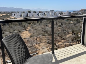 Un balcón con vistas a un paisaje desértico, vegetación escasa y edificios lejanos.