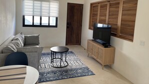 A living room with a sofa, a coffee table, a TV on a wooden cabinet, a ceiling fan, and a window with blinds. - BRIGHT & COZY 1-KING BEDROOM CASITA WITH QUEEN SLEEPER IN CENTRAL CERRITOS BEACH (Pescadero)