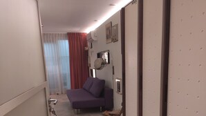 Un couloir étroit avec un lit, un climatiseur fixé au mur et une porte dotée d’une serrure et d’une clé.