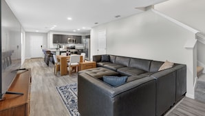 Ein modernes Wohnzimmer mit Ecksofa, einem Essbereich und einer Küche im Hintergrund.