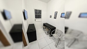 A small, modern room with a black desk, a chair, a small table, and a window with bars.
