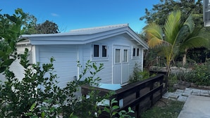 A white single-story house with a small porch, surrounded by lush greenery and a palm tree. - Garden Studio Retreat (Sint Michiel)
