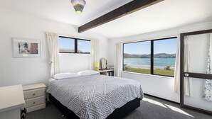 A bedroom with a bed, a bedside table, a lamp, a window with a view of the sea, and a ceiling light.