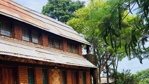 A rustic brick building with a corrugated metal roof, a small porch, and a stone retaining wall. - Deanshillsviewlodge (Chipata)