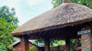 A rustic kitchen area with a thatched roof, brick walls, and a sign indicating the kitchen. - Deanshillsviewlodge (Chipata)