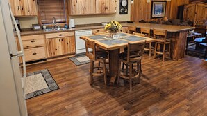 A kitchen with wooden cabinets, a central island with stools, a sink, and a clock on the wall.