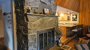 A stone fireplace with a metal screen, a wooden bar area, and a seating area with patterned cushions.