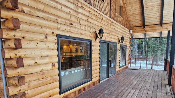 A wooden log cabin with large windows and a wooden deck.
