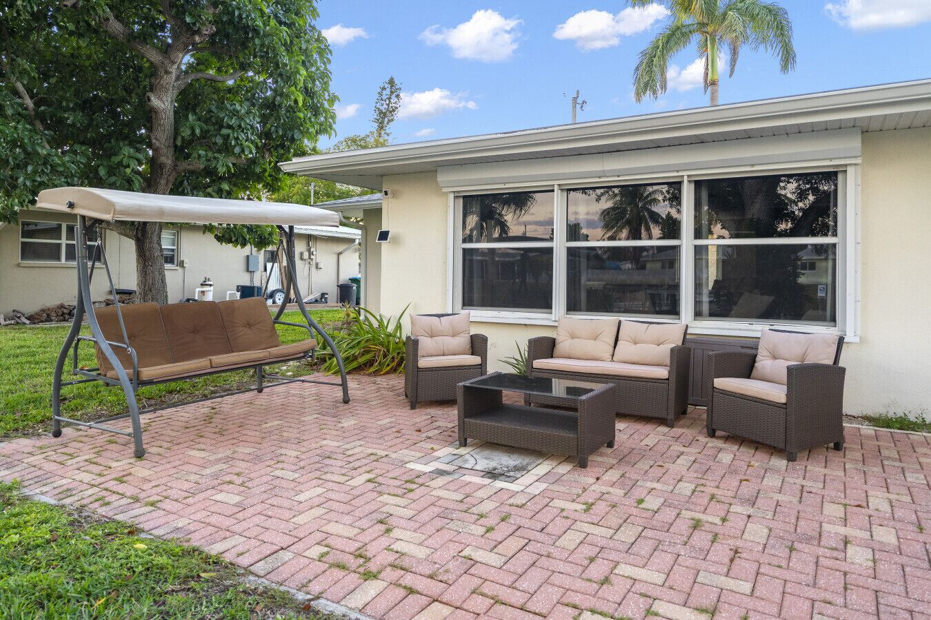 An outdoor patio with wicker furniture, a swing, and a covered bench.