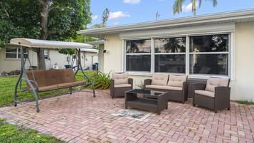 An outdoor patio with wicker furniture, a swing, and a covered bench.