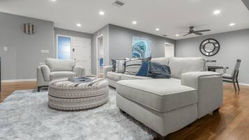 A modern living room with a grey sofa, ottoman, and armchair, a fluffy rug, and a ceiling fan.