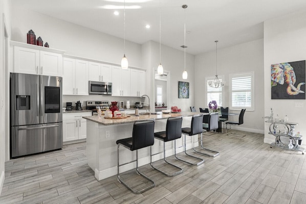 A modern kitchen with white cabinets, stainless steel appliances, a granite countertop, and a bar area with black barstools.