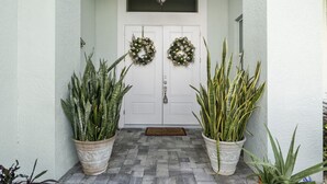 Una puerta principal con dos grandes macetas a cada lado, una puerta doble con una corona decorativa y una pequeña ventana encima de la puerta.