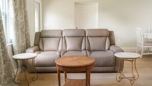 Un salon avec un canapé beige, deux petites tables rondes en bois et une table à manger blanche.