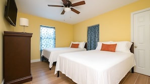 Une chambre d’hôtel avec deux lits, un ventilateur de plafond, une télévision et une commode en bois.