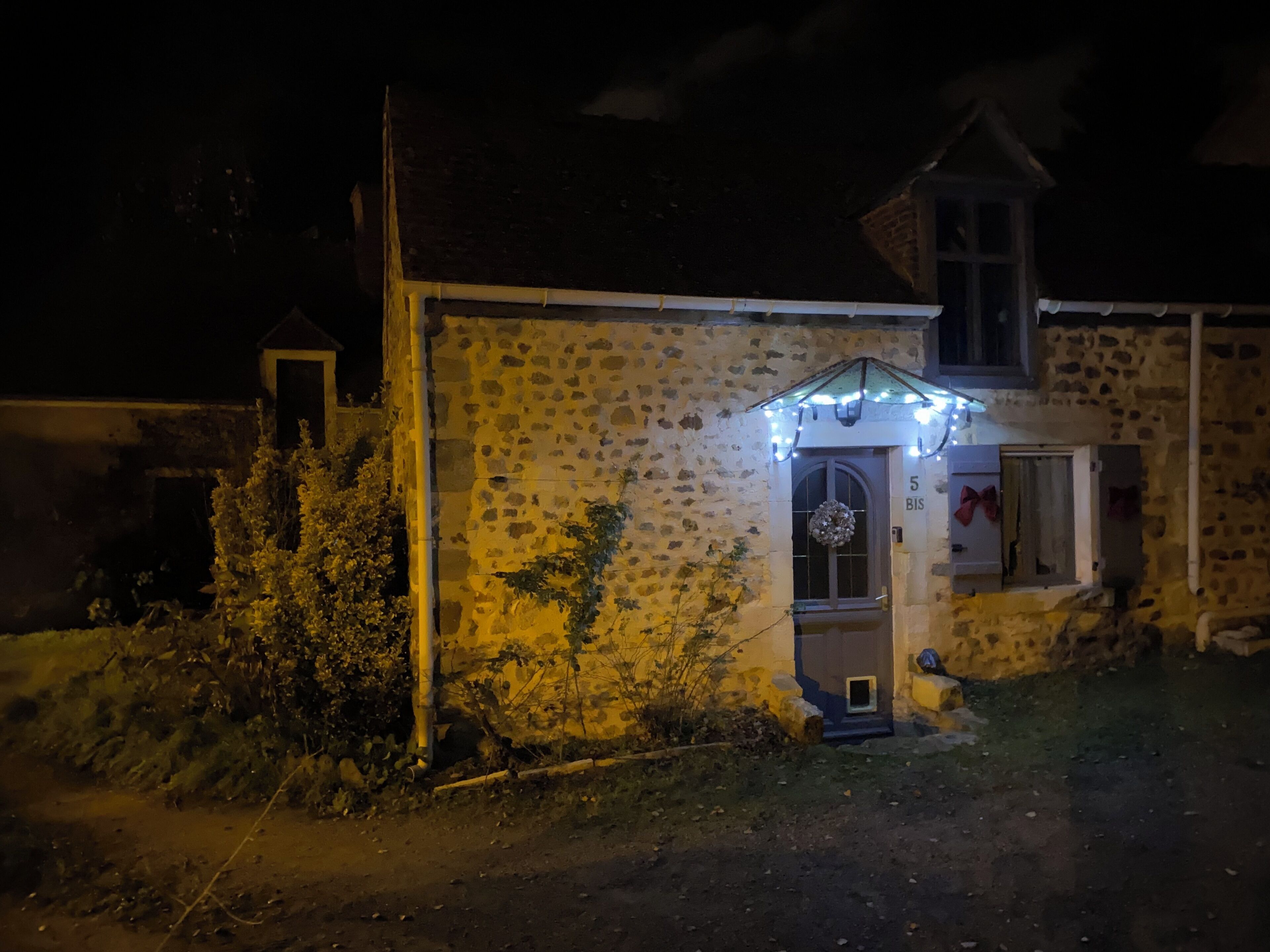 Un bâtiment en pierre avec un petit porche, une porte ornée d’une guirlande et le chiffre « 5 » au-dessus de la porte.